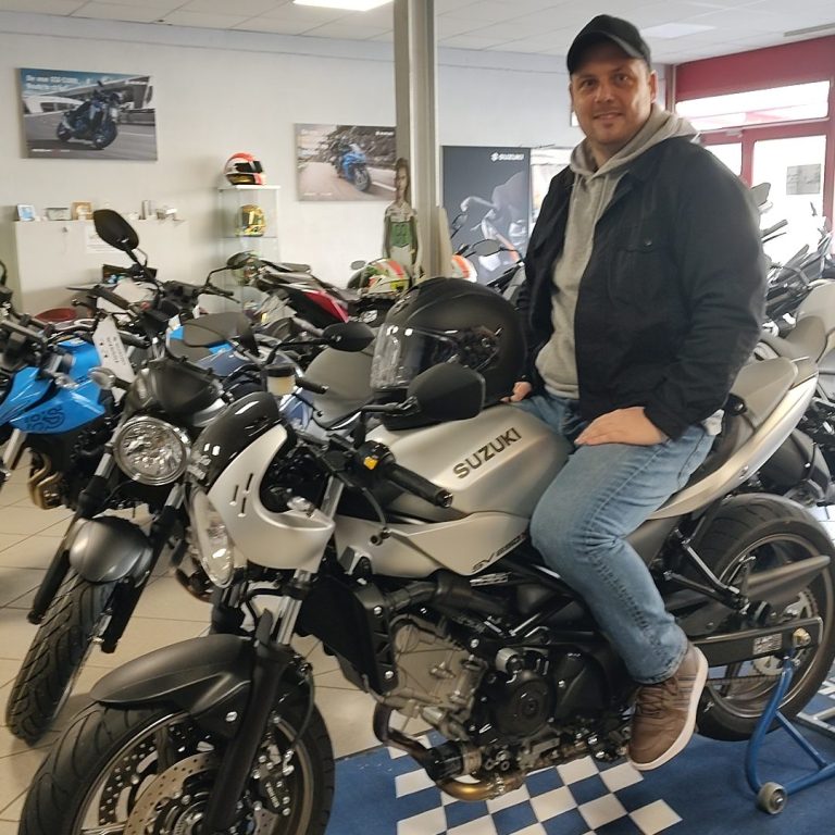 Mann sitzt auf einem silbernen Motorrad in einem Motorradhändlergeschäft.