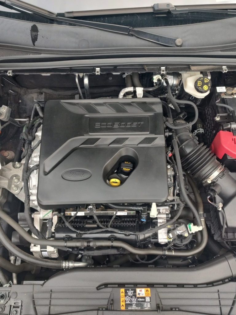 Motorraum mit einem schwarzen Motorblock und sichtbaren Komponenten.