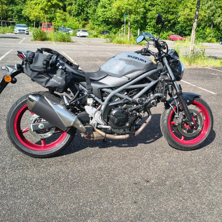 Frau sitzt auf einem Motorrad in einem Verkaufsraum, umgeben von Helmen und Zubehör.