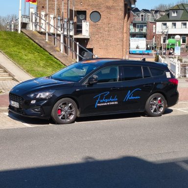 Schwarzer Kombi mit blauer Unterschrift auf der Seite, geparkt in einem Wohngebiet.